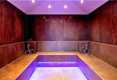 Ein eleganter Wellnessbereich mit einem beheizten Wasserbecken und LED-Beleuchtung. Die Wände sind in warmen Brauntönen gehalten und schaffen eine entspannende Atmosphäre.