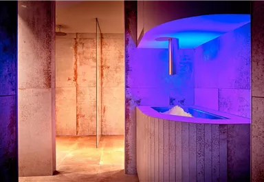Ein moderner Spa-Bereich mit sanftem, buntem Licht. Die Wände sind aus Beton und es gibt eine stilvolle Liegefläche.