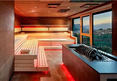 Eine moderne Sauna mit hellem Holz und stimmungsvollem Licht. Das große Fenster bietet einen Blick auf die Landschaft.