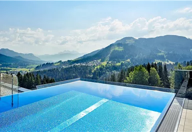 Ein Infinity-Pool mit atemberaubendem Blick auf die Berge und die Landschaft. Der Himmel ist klar und die Sonne scheint.