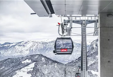 Eine Seilbahn auf einem schneebedeckten Berg mit beeindruckender Berglandschaft im Hintergrund. Der Himmel ist klar und die Umgebung wirkt winterlich und frisch.