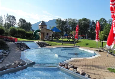 Ein schöner Poolbereich mit einem Spielplatz im Hintergrund. Die Umgebung ist grün und einladend, perfekt für Familien.
