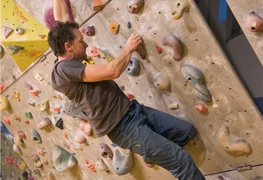 A climber navigating a climbing wall with various grips. The wall is colorful and has numerous small holds.