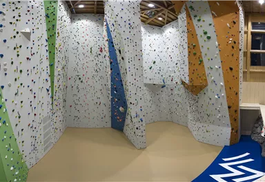 A modern climbing wall with colorful holds and various difficulty levels. The room is well-lit and provides space for climbers.
