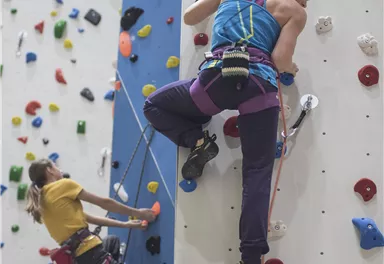 Two people are climbing a climbing wall. One person is belaying the other with a rope.
