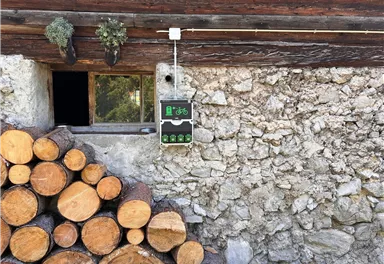 An einer steinernen Wand liegt ein Holzstapel. Über dem Fenster hängt ein Schild mit einem Fahrrad-Symbol.