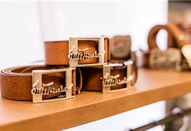 Three leather belts with shiny buckles lie on a shelf. The belts have a warm brown color and are stylishly presented.