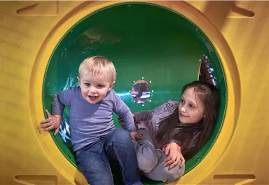 Ein kleiner Junge und ein Mädchen spielen zusammen in einem bunten Tunnel. Beide haben Freude und lachen.