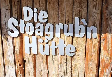 A wooden wall with the inscription "Die Stoagrub’n Hütte". The letters are white and highlighted.