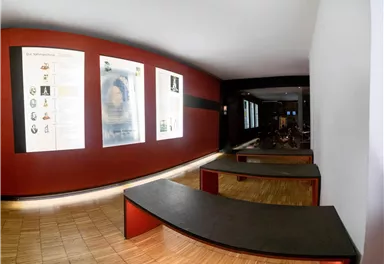 Ein Museumsausstellungsraum mit roten Wänden und Informationsst Boards. Es gibt eine Holzfußböden und moderne Sitzgelegenheiten.