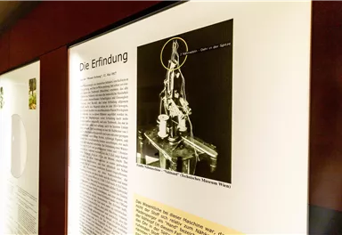 Eine Ausstellung über eine Erfindung mit einem Bild und beschreibendem Text. Das Bild zeigt eine technische Vorrichtung auf einem Schreibtisch.