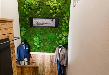 A stylish staircase descent with a green wall and wood paneling. Men's clothing is hanging on the sides.