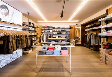 A modern clothing store with neatly arranged shelves and a variety of clothing. In the center stands a glass table with folded tops.