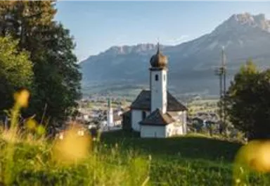 A picturesque church on a hill with an impressive mountain backdrop in the background. The surroundings are green and blooming, ideal for nature lovers.