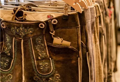 A selection of traditional lederhosen hangs on wooden hangers. The trousers are intricately decorated and made from high-quality material.