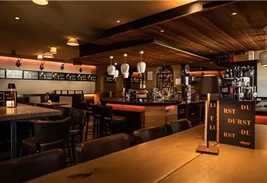 A cozy bar with wooden interior and dimmable lighting. The counter area is well stocked and inviting.