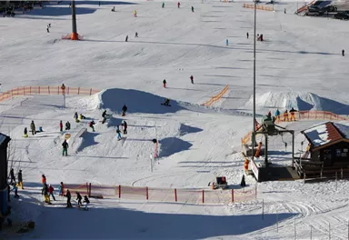Eine lebhafte Wintersportlandschaft mit vielen Leuten, die Ski fahren und snowboarden. Der Schnee ist frisch und die Atmosphäre ist fröhlich.