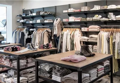 A modern clothing store with shelves full of clothes. Folded textiles are laid out on the tables and shoes are ready.