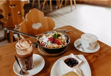 Ein köstliches Frühstück mit einer bunten Schüssel Granola, frischen Früchten und Joghurt. Dazu gibt es einen Cappuccino und eine Tasse Kaffee mit Schlagsahne.