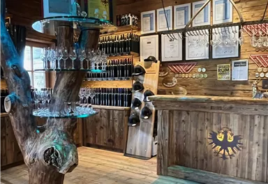 A rustic wooden bar with a unique tree as a table stand. Various awards and bottles are hanging on the wall.