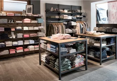 A modern clothing store with neatly stacked garments on shelves and tables. The color palette includes soft tones, creating an inviting atmosphere.