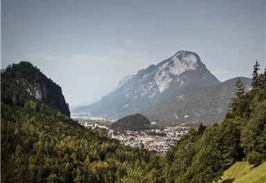 A picturesque mountain landscape with green forests and rugged peaks. In the valley, a small town is visible.