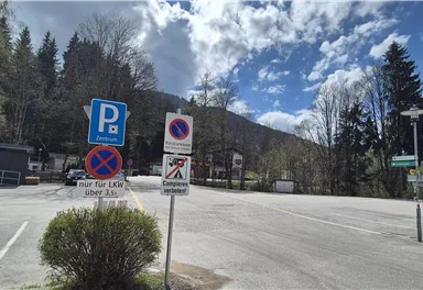 A parking lot with various traffic signs in a green environment. The sky is partly cloudy and the parking lot appears to be calm.