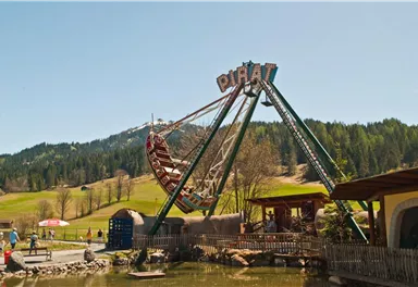 A carousel in an amusement park with a picturesque mountain landscape in the background. Visitors enjoy the attraction on a sunny day.