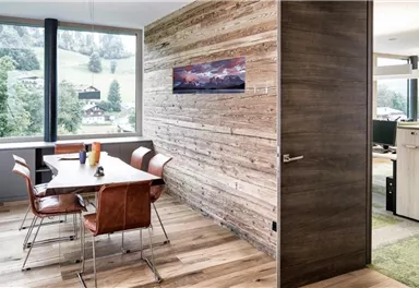 A modern office space with a large window and a view of nature. The table is equipped with elegant chairs and the walls are made of wood.