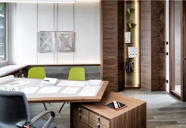 A modern office with a large table and comfortable chairs. The walls are painted in light wood and gray tones, and there is plenty of natural light.