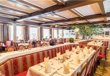 A cozy restaurant with elegant tables and red benches. The light floods through large windows, creating an inviting atmosphere.