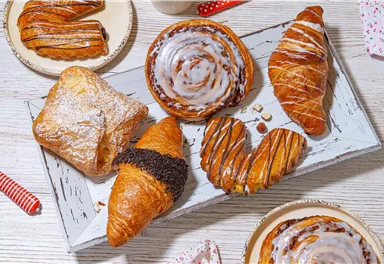A appetizing selection of pastries on a rustic tray. The treats include croissants, cinnamon rolls, and filled pastries.