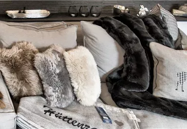 Ein gemütliches Sofa mit mehreren dekorativen Kissen und einer weichen Decke. Die Einrichtung strahlt eine einladende und entspannte Atmosphäre aus.