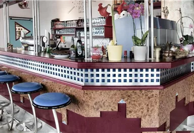Eine stilvolle Bar mit blauen Hockern und bunten Dekorationen. Die Theke ist modern gestaltet und bietet eine einladende Atmosphäre.