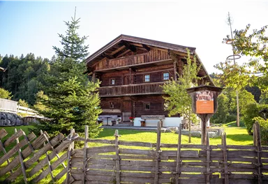 A traditional wooden house in the midst of a green environment. There is a fenced garden with trees and a view of nature.