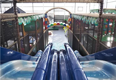 Eine Rutschbahn in einem Indoor-Spielplatz mit bunten Dekorationen. Der Blick von der Rutschbahn zeigt die Spielbereiche im Hintergrund.