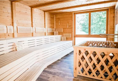 Ein heller Wellnessraum mit hölzernen Bänken und großen Fenstern. Der Raum strahlt Ruhe und Entspannung aus.
