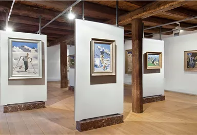 Ein Kunstmuseum mit mehreren Bilderrahmen auf weißen Wänden. Der Raum hat Holzböden und eine warme Atmosphäre.