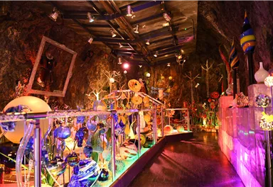 A colorful room with artistic glass sculptures and colored light. The walls are made of rock, creating a unique atmosphere.