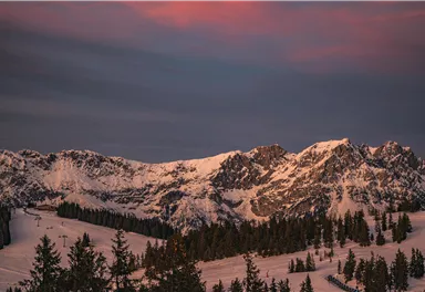 Eine beeindruckende Berglandschaft mit schneebedeckten Gipfeln und dunklem Himmel. Sanfte Farben der Dämmerung verleihen der Szene einen besonderen Charme.
