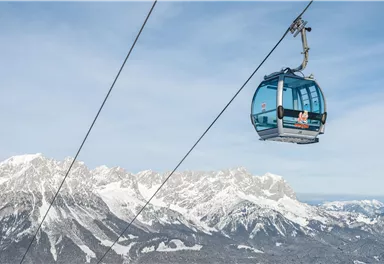 A cable car glides over snow-covered mountains. The clear sky and the majestic landscape convey a sense of freedom.