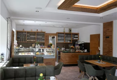 Ein modernes Café mit Holzinterieur und gemütlichen Sitzbereichen. Die Auslage zeigt eine Auswahl an Speisen und Getränken.