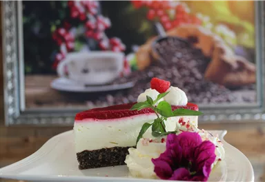 Ein köstliches Stück Erdbeertorte auf einem weißen Teller. Im Hintergrund sind Kaffeebohnen und eine Tasse zu sehen.
