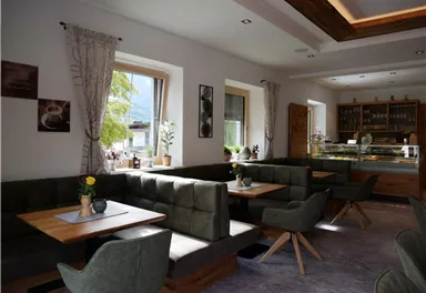 Ein modernes Café mit gemütlichen Sitzgelegenheiten und großen Fenstern. Die Einrichtung ist hell und einladend, ideal für entspannte Besuche.