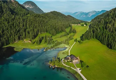 A picturesque landscape with a clear lake and lush green meadows. In the background, gentle hills and mountains rise.