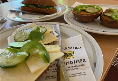 A plate with filled rolls, topped with cucumbers and peppers. In the background, there are more rolls and a printout from a bakery visible.