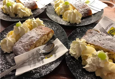 Four plates with delicious apple strudel, plenty of whipped cream, and a decorative green grape. The plates are arranged on a tray, giving the dessert an inviting appearance.
