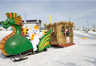 A colorful sled in the shape of a dragon rides through the snow. A cheerful snowman sits in the golden carriage of the sled.
