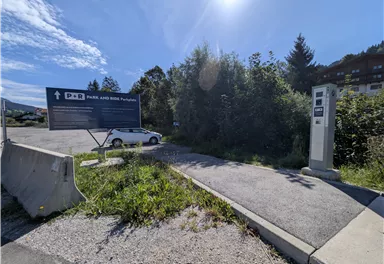 A parking lot with a sign indicating an entrance. In the background, there are trees and the sky is clear and blue.
