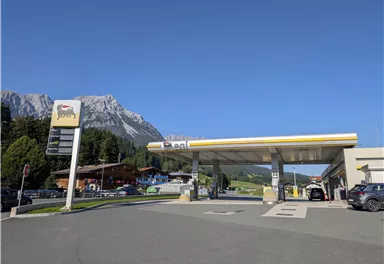 Eine Tankstelle vor einer malerischen Berglandschaft. Der Himmel ist klar und blau.